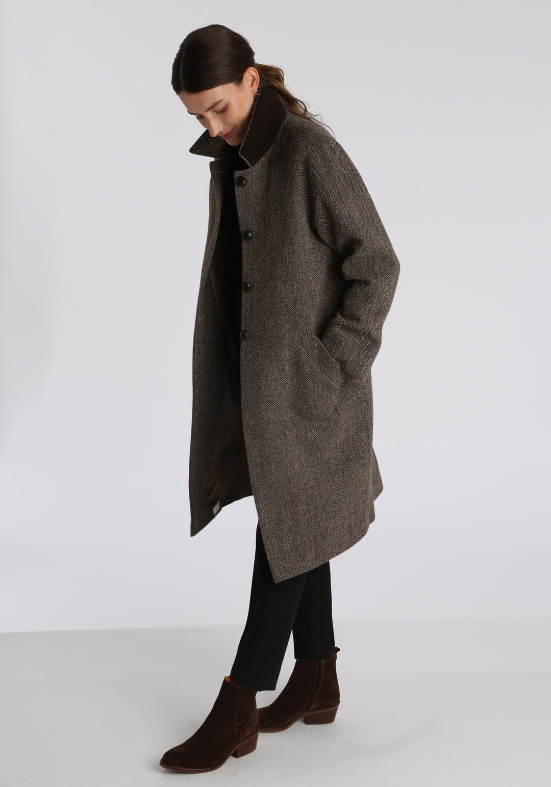 Model wearing the Dari coat in heather herringbone Harris Tweed, a relaxed cocoon-shaped style with raglan sleeves, finished with leather trim.