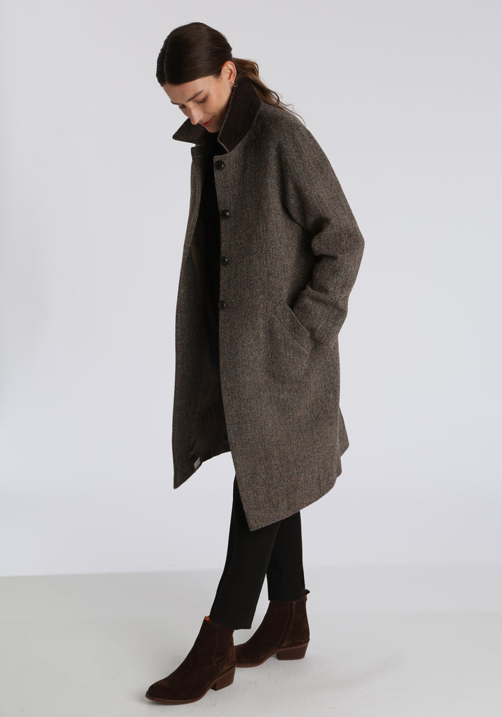 Model wearing the Dari coat in heather herringbone Harris Tweed, a relaxed cocoon-shaped style with raglan sleeves, finished with leather trim.
