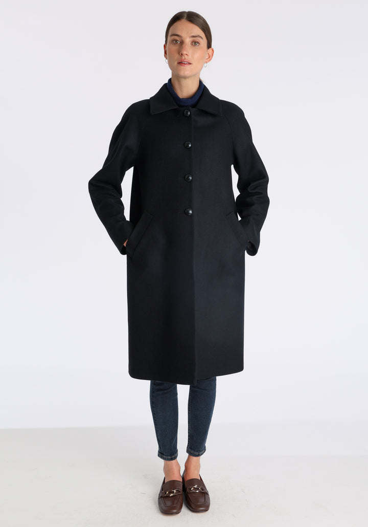 Model wearing the Dari coat in black cashmere blend, a relaxed cocoon-shaped style with raglan sleeves, finished with suede trim.