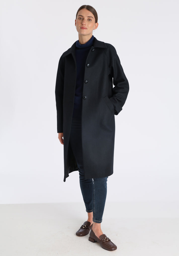 Model wearing the Dari coat in black cashmere blend, a relaxed cocoon-shaped style with raglan sleeves, finished with suede trim.