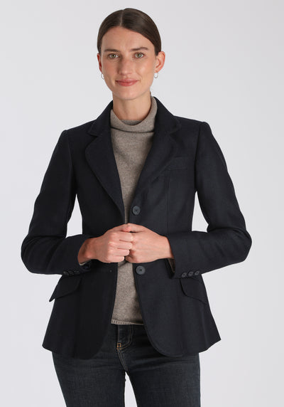 Model wearing the Hacking jacket in a navy herringbone lambswool, a slim fit style with notched lapels, angled hip pockets, and a single back vent, inspired by traditional equestrian tailoring.