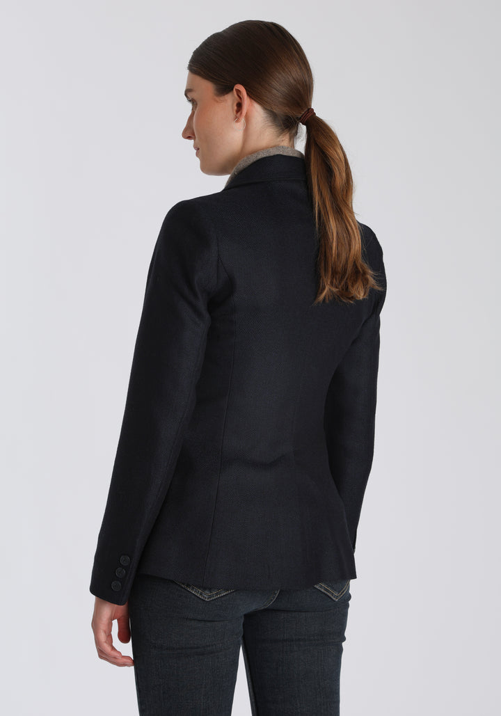 Model wearing the Hacking jacket in a navy herringbone lambswool, a slim fit style with notched lapels, angled hip pockets, and a single back vent, inspired by traditional equestrian tailoring.