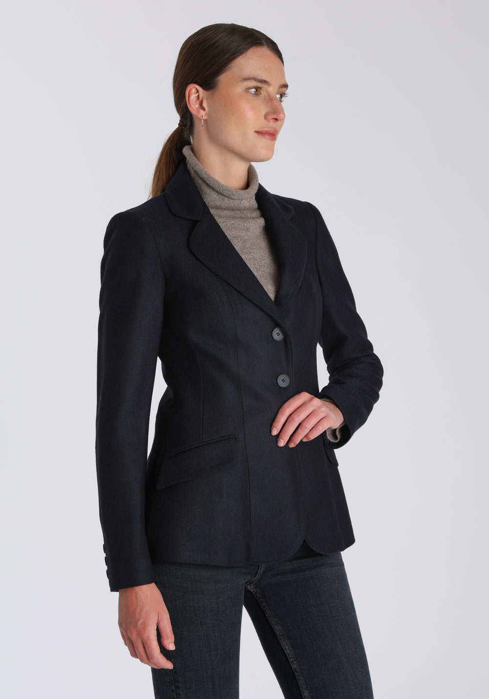 Model wearing the Hacking jacket in a navy herringbone lambswool, a slim fit style with notched lapels, angled hip pockets, and a single back vent, inspired by traditional equestrian tailoring.