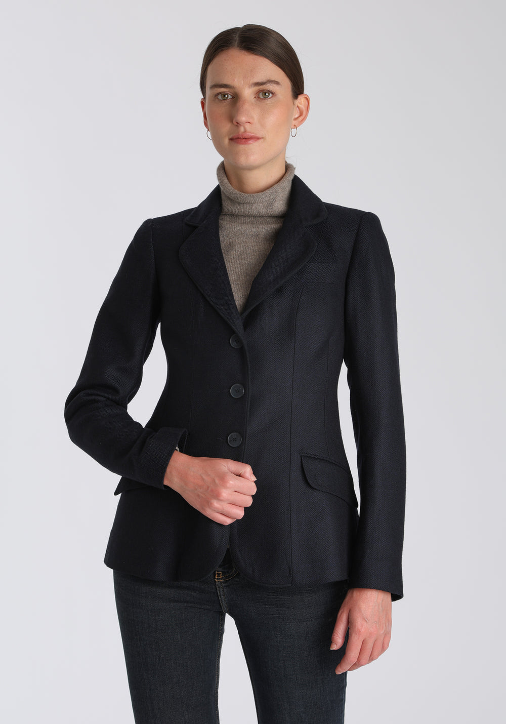 Model wearing the Hacking jacket in a navy herringbone lambswool, a slim fit style with notched lapels, angled hip pockets, and a single back vent, inspired by traditional equestrian tailoring.