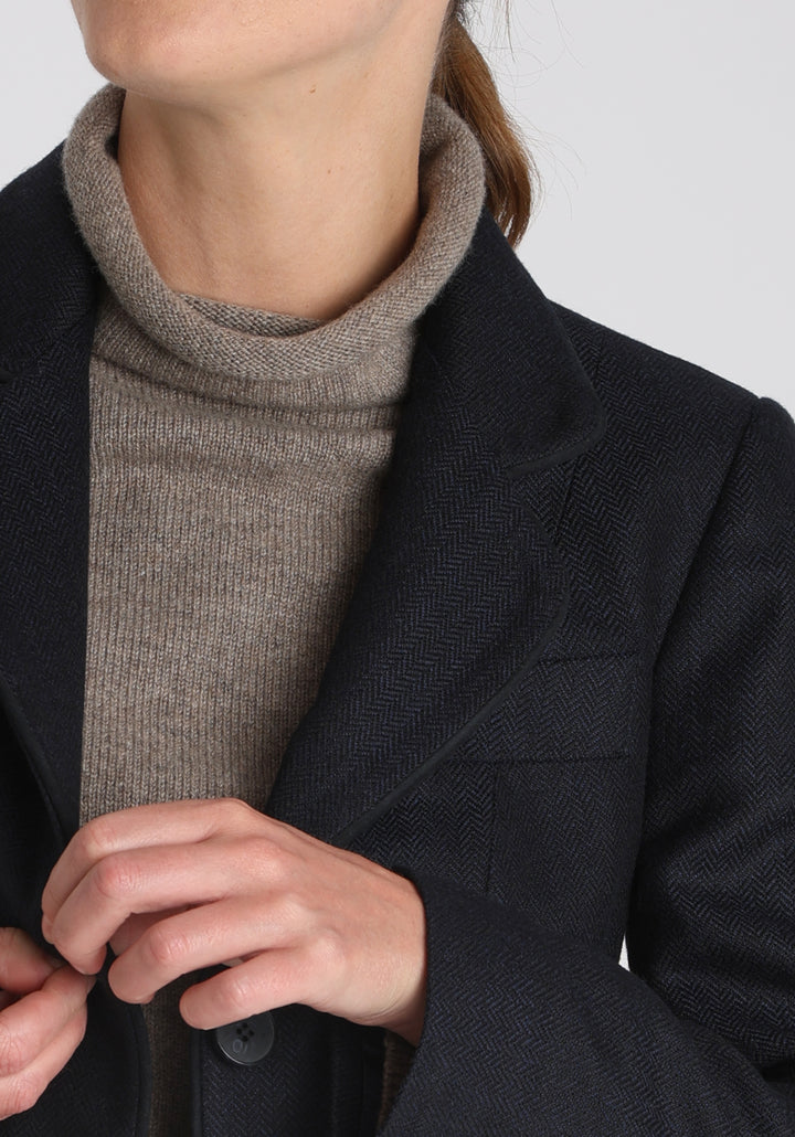 Model wearing the Hacking jacket in a navy herringbone lambswool, a slim fit style with notched lapels, angled hip pockets, and a single back vent, inspired by traditional equestrian tailoring.