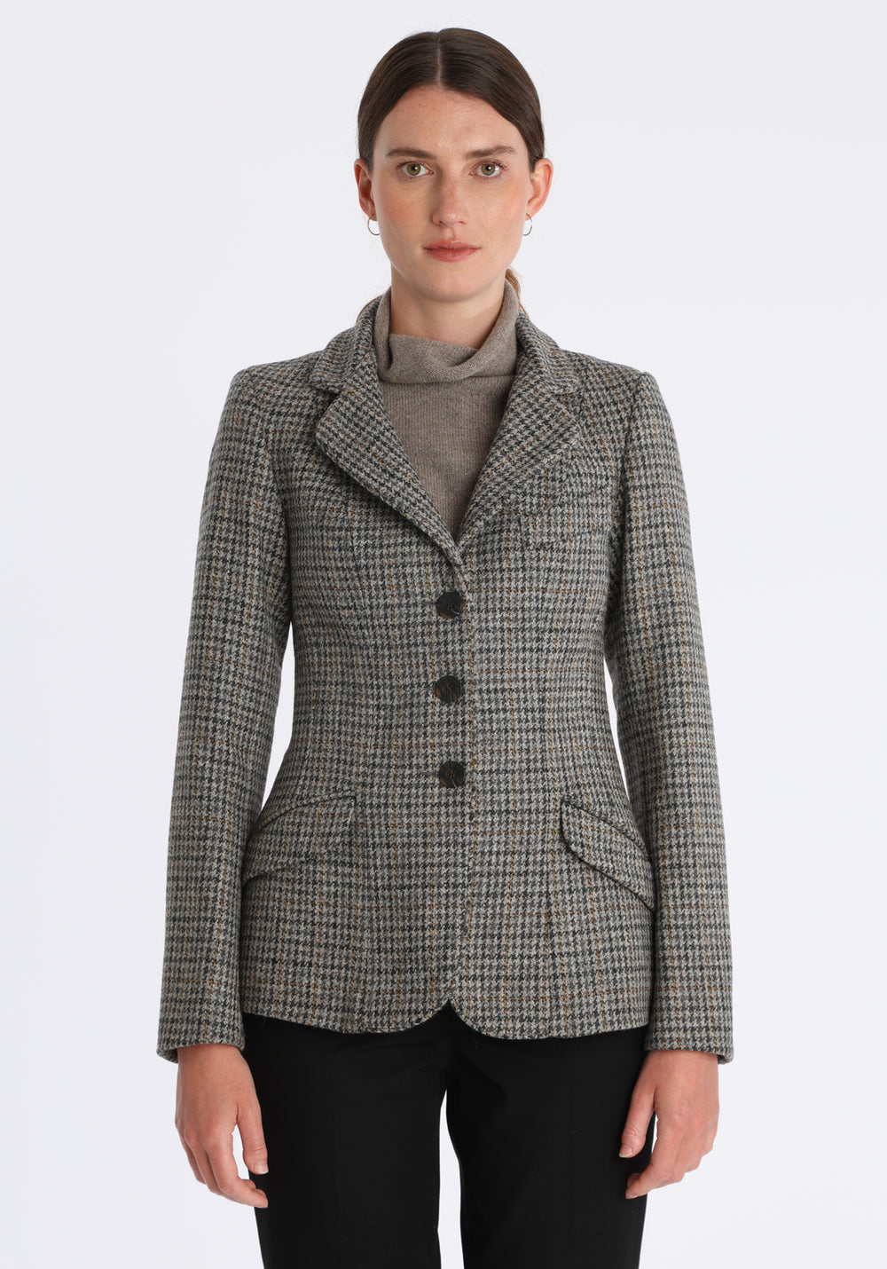 Model wearing the Hacking jacket in a stone grey and ochre dogtooth wool, a slim fit style with notched lapels, angled hip pockets, and a single back vent, inspired by traditional equestrian tailoring.