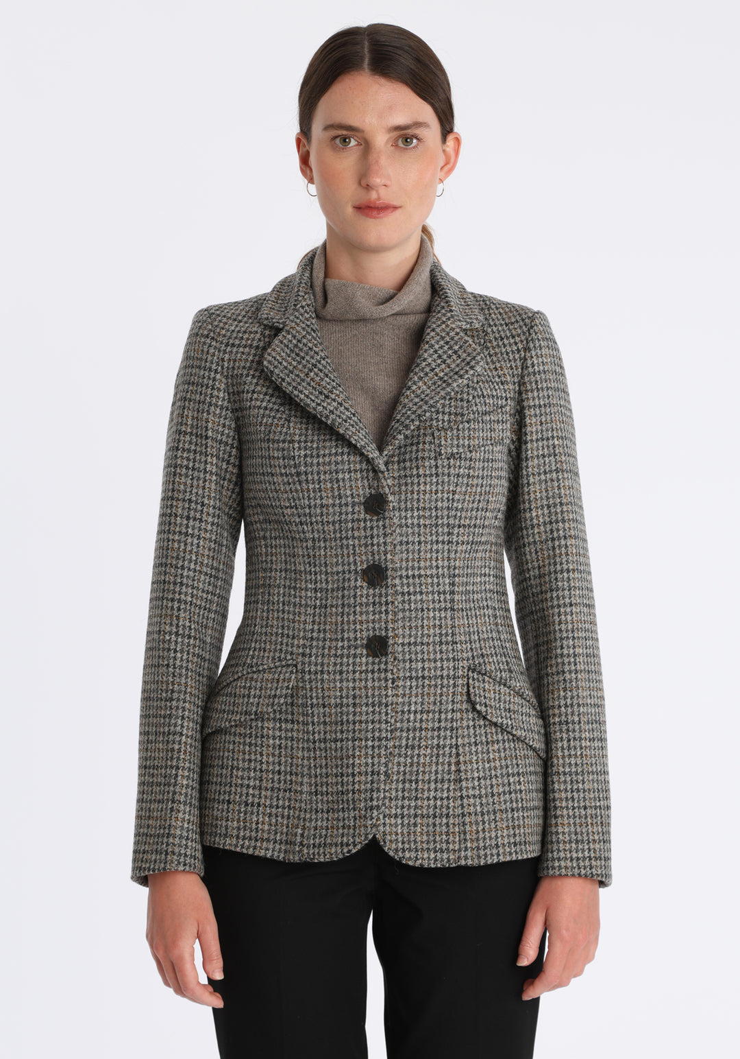 Model wearing the Hacking jacket in a stone grey and ochre dogtooth wool, a slim fit style with notched lapels, angled hip pockets, and a single back vent, inspired by traditional equestrian tailoring.