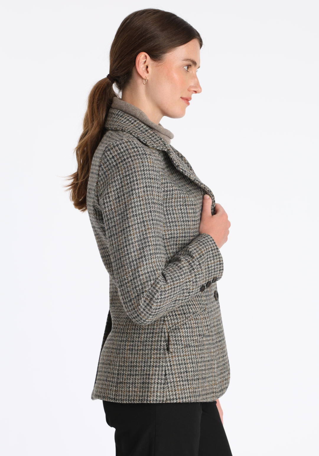 Model wearing the Hacking jacket in a stone grey and ochre dogtooth wool, a slim fit style with notched lapels, angled hip pockets, and a single back vent, inspired by traditional equestrian tailoring.