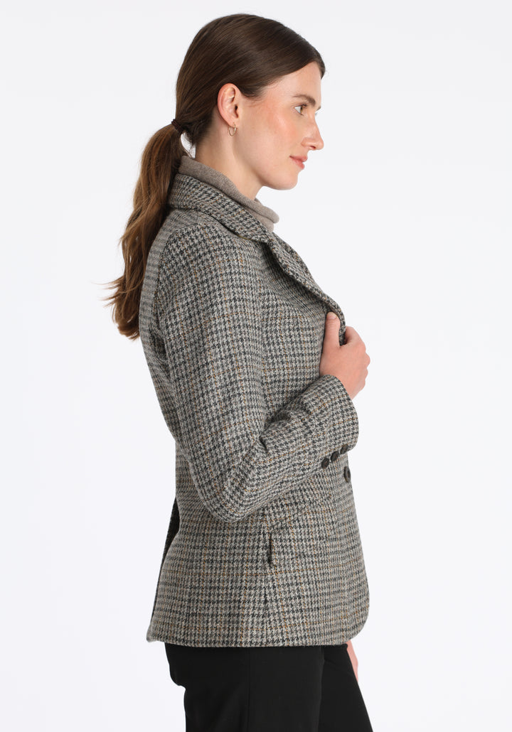Model wearing the Hacking jacket in a stone grey and ochre dogtooth wool, a slim fit style with notched lapels, angled hip pockets, and a single back vent, inspired by traditional equestrian tailoring.