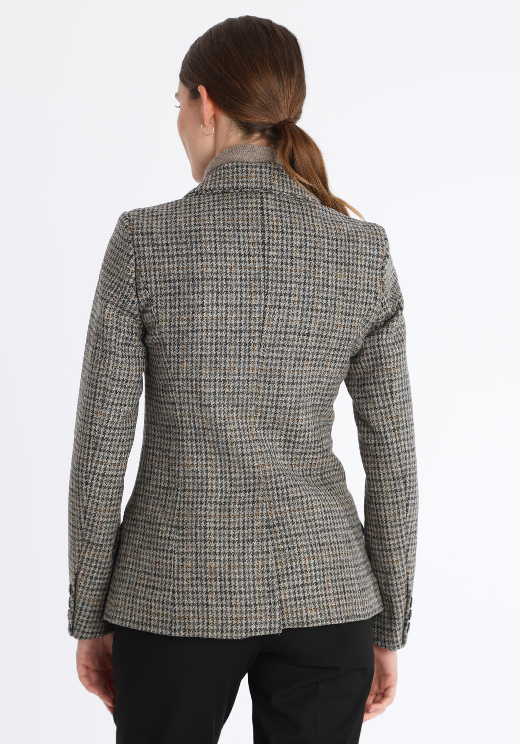Model wearing the Hacking jacket in a stone grey and ochre dogtooth wool, a slim fit style with notched lapels, angled hip pockets, and a single back vent, inspired by traditional equestrian tailoring.