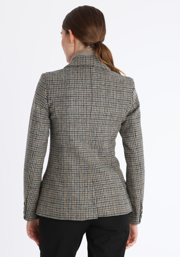 Model wearing the Hacking jacket in a stone grey and ochre dogtooth wool, a slim fit style with notched lapels, angled hip pockets, and a single back vent, inspired by traditional equestrian tailoring.