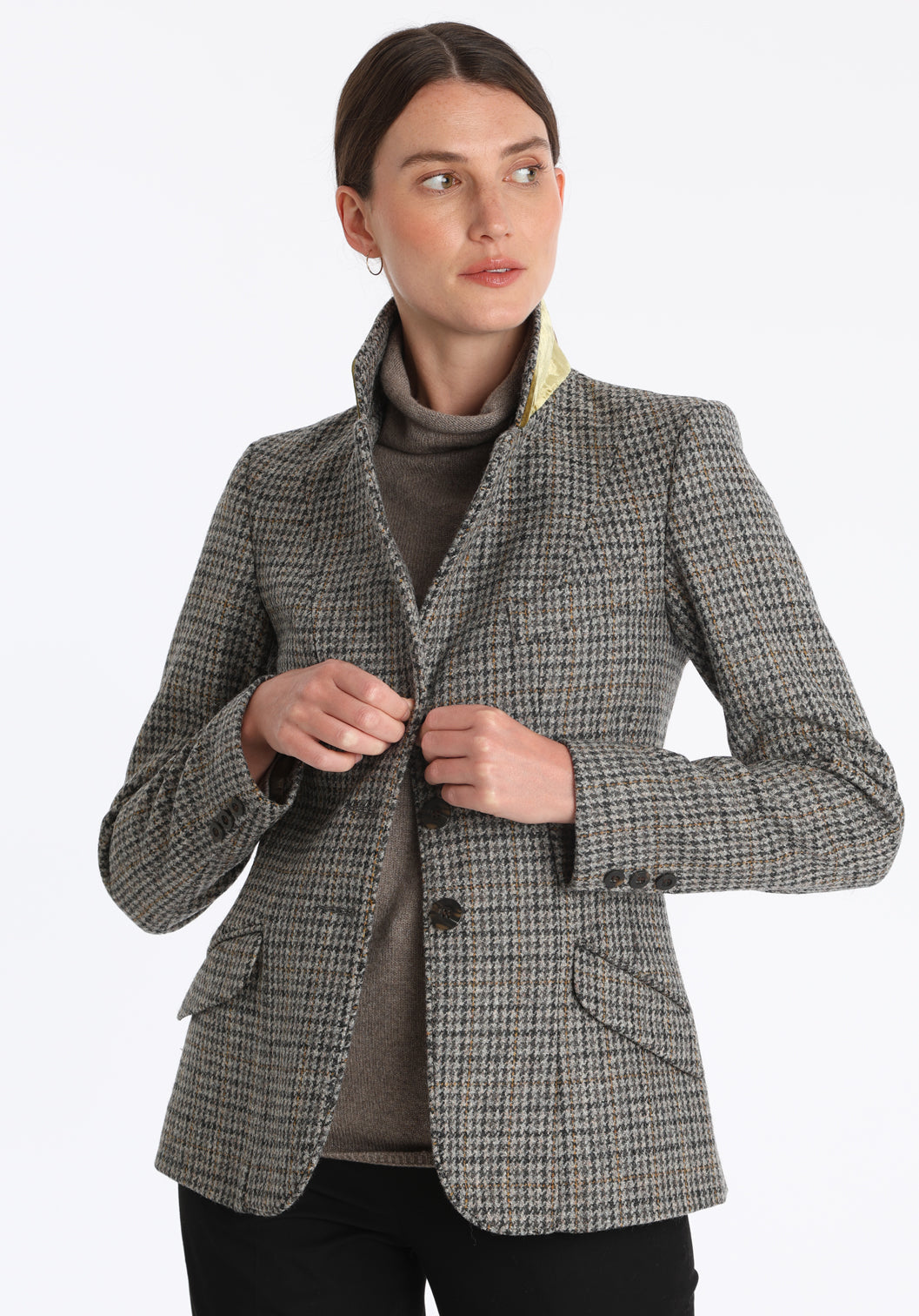 Model wearing the Hacking jacket in a stone grey and ochre dogtooth wool, a slim fit style with notched lapels, angled hip pockets, and a single back vent, inspired by traditional equestrian tailoring.