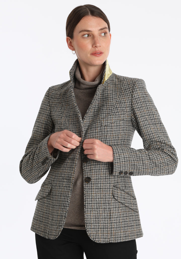Model wearing the Hacking jacket in a stone grey and ochre dogtooth wool, a slim fit style with notched lapels, angled hip pockets, and a single back vent, inspired by traditional equestrian tailoring.
