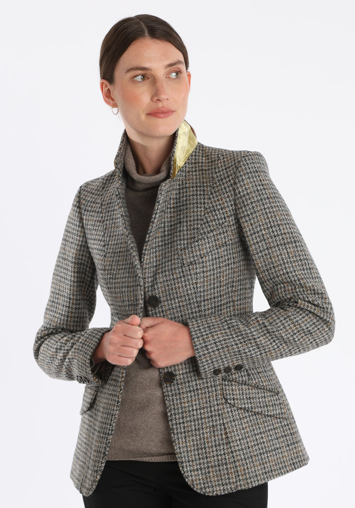 Model wearing the Hacking jacket in a stone grey and ochre dogtooth wool, a slim fit style with notched lapels, angled hip pockets, and a single back vent, inspired by traditional equestrian tailoring.