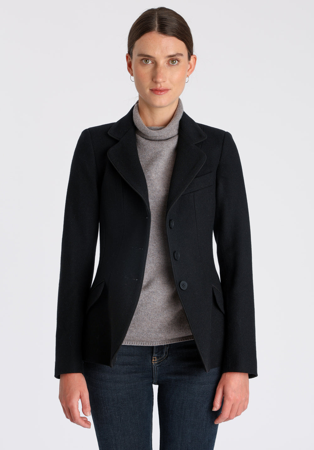 Model wearing the Hacking jacket in black textured merino wool, a slim fit style with notched lapels, angled hip pockets, and a single back vent, inspired by traditional equestrian tailoring.