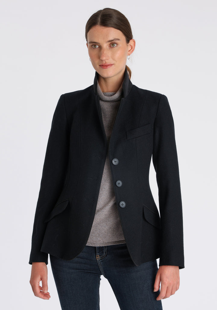 Model wearing the Hacking jacket in black textured merino wool, a slim fit style with notched lapels, angled hip pockets, and a single back vent, inspired by traditional equestrian tailoring.