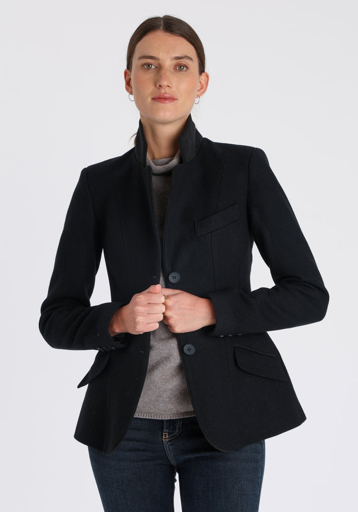 Model wearing the Hacking jacket in black textured merino wool, a slim fit style with notched lapels, angled hip pockets, and a single back vent, inspired by traditional equestrian tailoring.