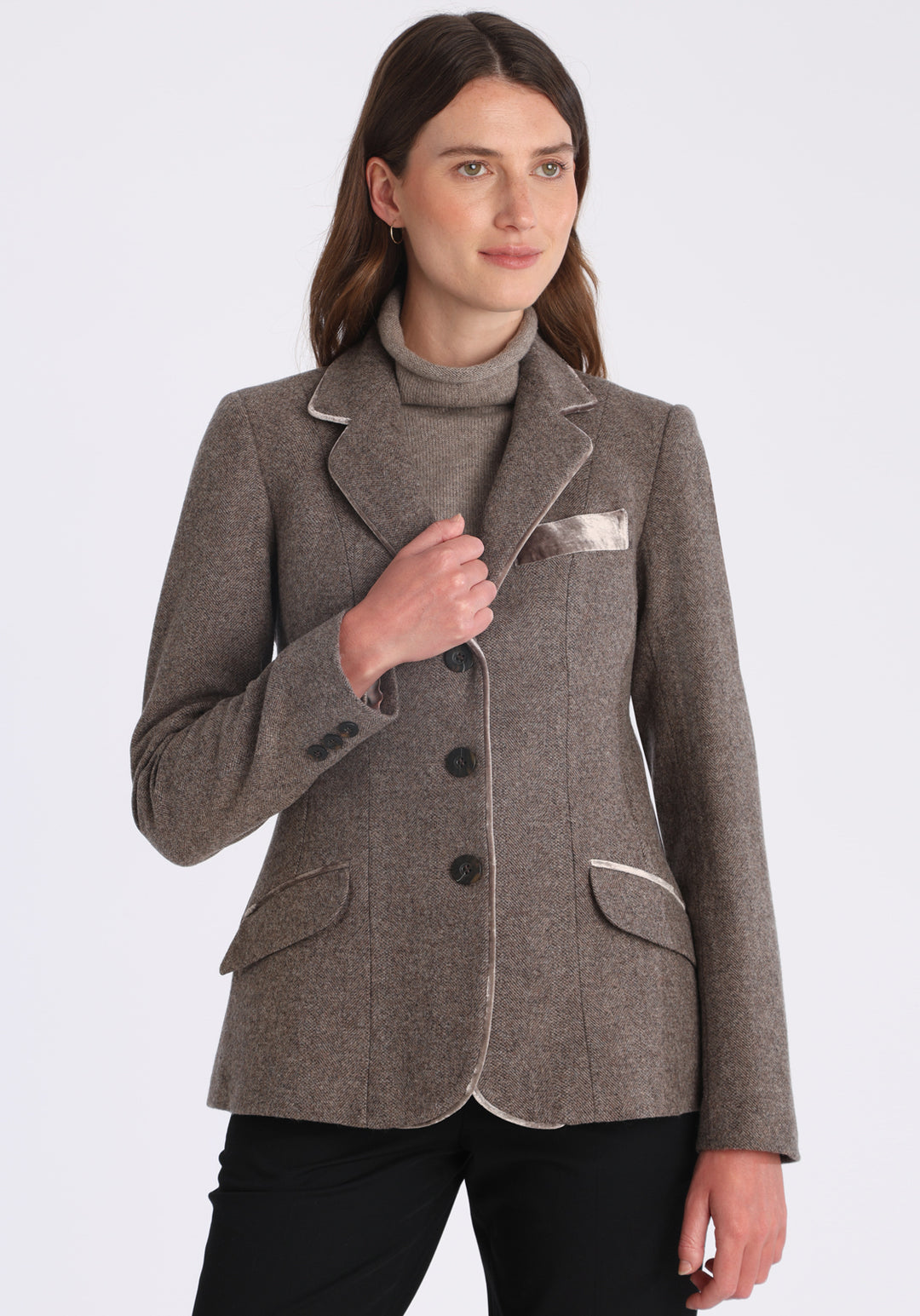Model wearing the Hacking jacket in a cool mallow taupe herringbone lambswool, a slim fit style with notched lapels, angled hip pockets, and a single back vent, inspired by traditional equestrian tailoring.