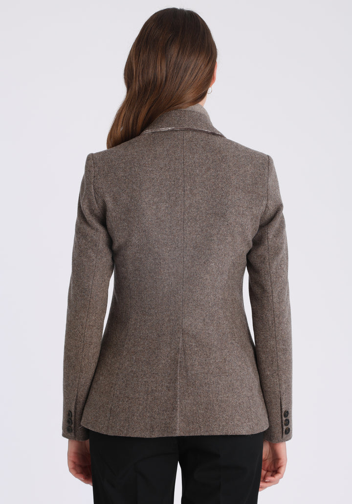 Model wearing the Hacking jacket in a cool mallow taupe herringbone lambswool, a slim fit style with notched lapels, angled hip pockets, and a single back vent, inspired by traditional equestrian tailoring.