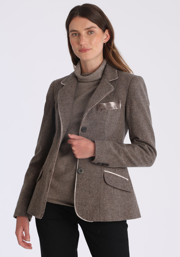 Model wearing the Hacking jacket in a cool mallow taupe herringbone lambswool, a slim fit style with notched lapels, angled hip pockets, and a single back vent, inspired by traditional equestrian tailoring.