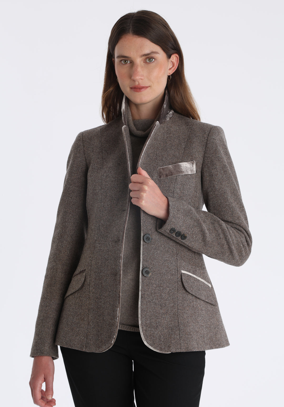 Model wearing the Hacking jacket in a cool mallow taupe herringbone lambswool, a slim fit style with notched lapels, angled hip pockets, and a single back vent, inspired by traditional equestrian tailoring.