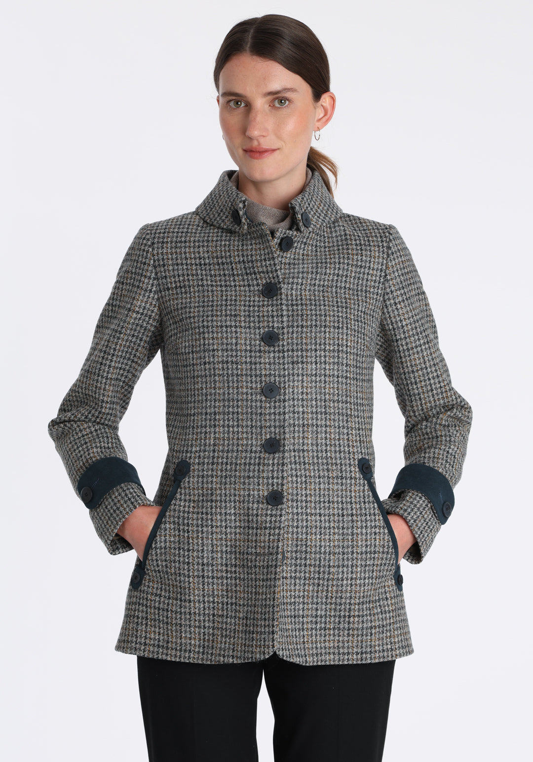 Model wearing the Hendre jacket in grey and ochre dogtooth check, a structured style with a high collar, reversible suede cuff bands, and a back belt for versatile styling.