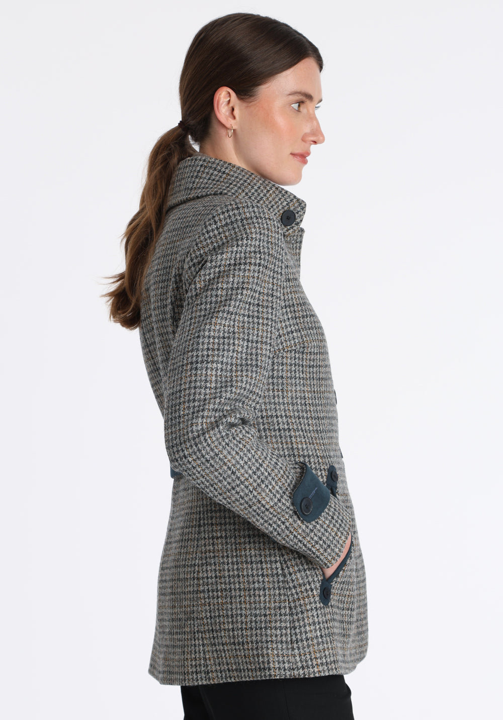Model wearing the Hendre jacket in grey and ochre dogtooth check, a structured style with a high collar, reversible suede cuff bands, and a back belt for versatile styling.
