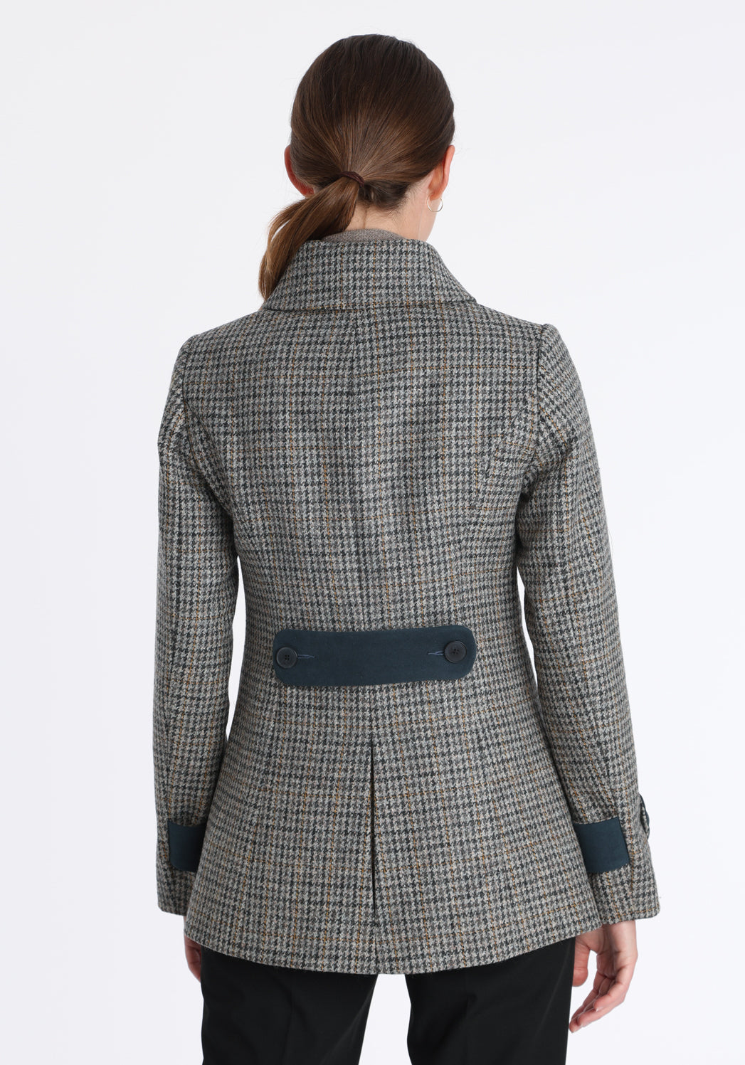 Model wearing the Hendre jacket in grey and ochre dogtooth check, a structured style with a high collar, reversible suede cuff bands, and a back belt for versatile styling.