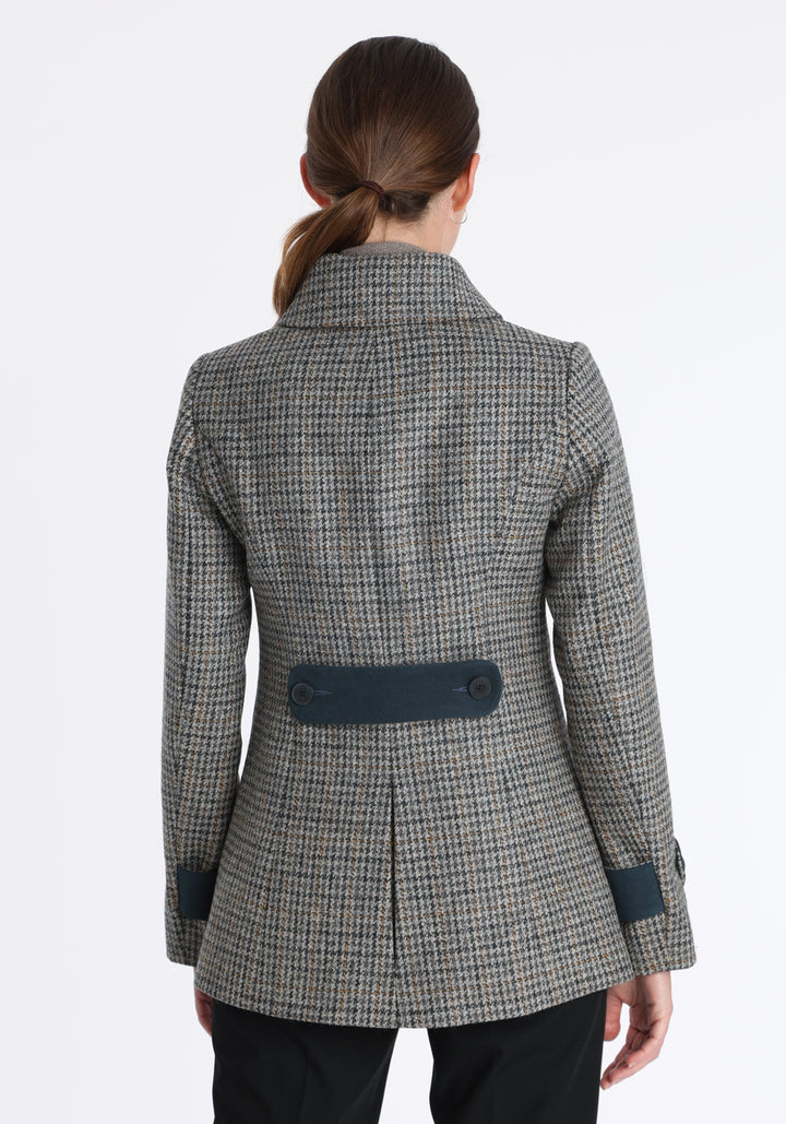 Model wearing the Hendre jacket in grey and ochre dogtooth check, a structured style with a high collar, reversible suede cuff bands, and a back belt for versatile styling.