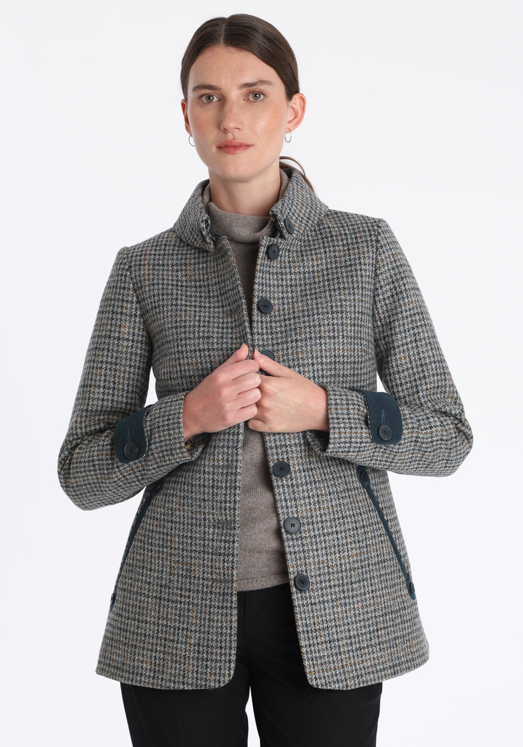 Model wearing the Hendre jacket in grey and ochre dogtooth check, a structured style with a high collar, reversible suede cuff bands, and a back belt for versatile styling.