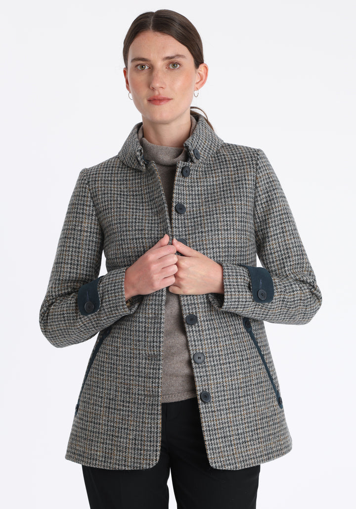 Model wearing the Hendre jacket in grey and ochre dogtooth check, a structured style with a high collar, reversible suede cuff bands, and a back belt for versatile styling.