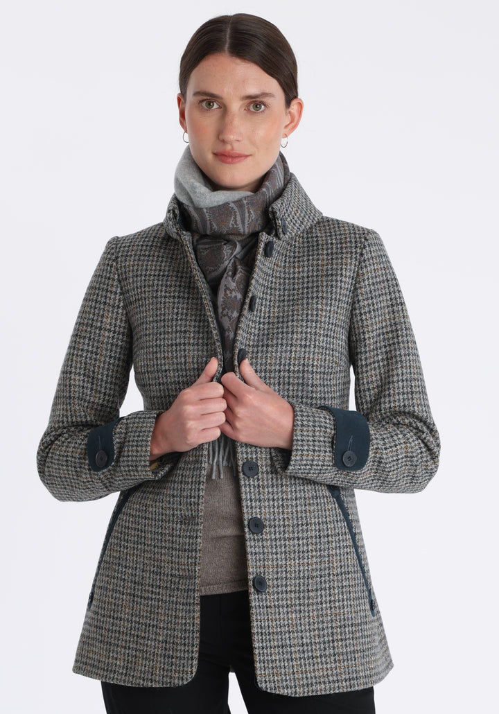 Model wearing the Hendre jacket in grey and ochre dogtooth check, a structured style with a high collar, reversible suede cuff bands, and a back belt for versatile styling.