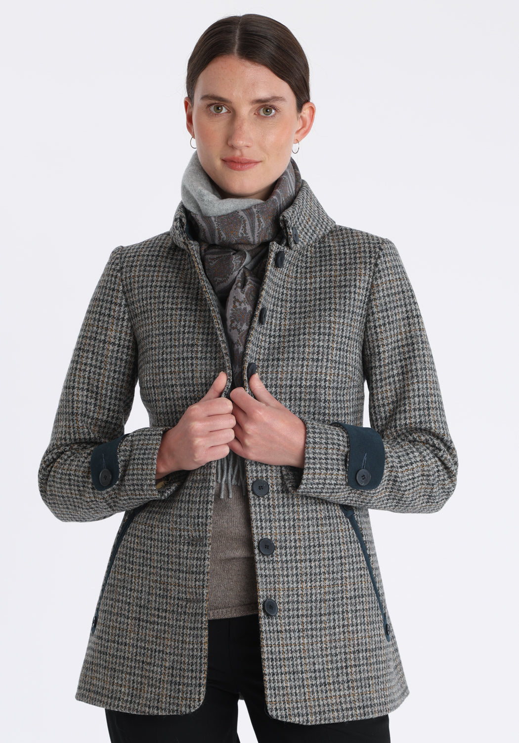 Model wearing the Hendre jacket in grey and ochre dogtooth check, a structured style with a high collar, reversible suede cuff bands, and a back belt for versatile styling.