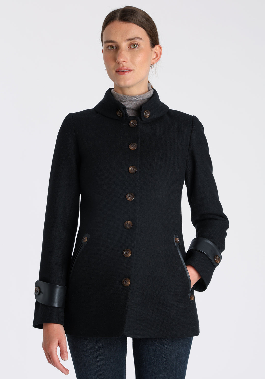 Model wearing the Hendre jacket in black textured wool, a structured style with a high collar, reversible leather cuff bands, and a back belt for versatile styling.