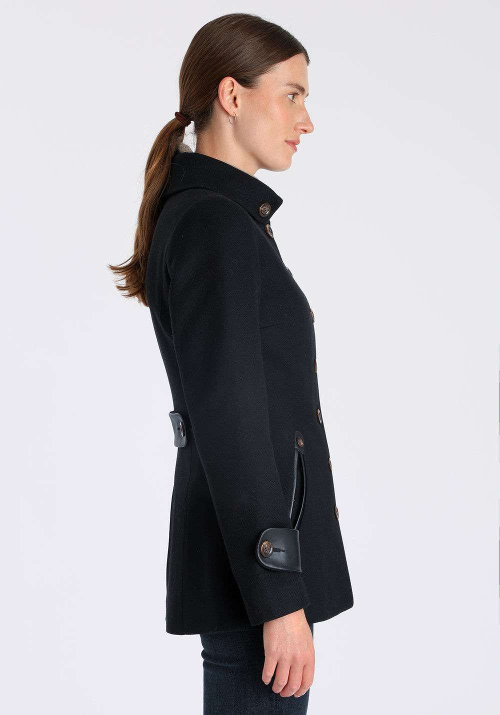 Model wearing the Hendre jacket in black textured wool, a structured style with a high collar, reversible leather cuff bands, and a back belt for versatile styling.