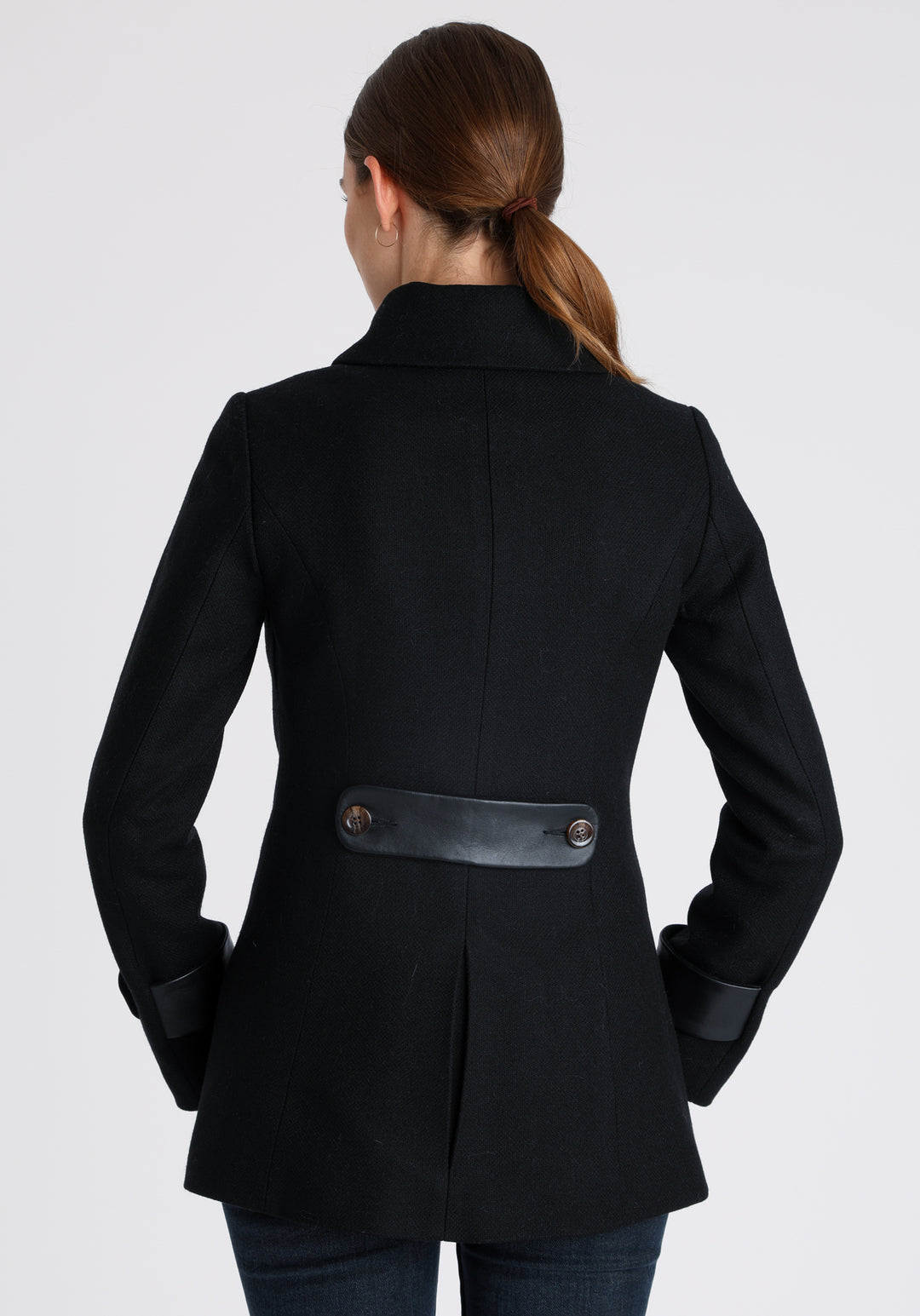 Model wearing the Hendre jacket in black textured wool, a structured style with a high collar, reversible leather cuff bands, and a back belt for versatile styling.