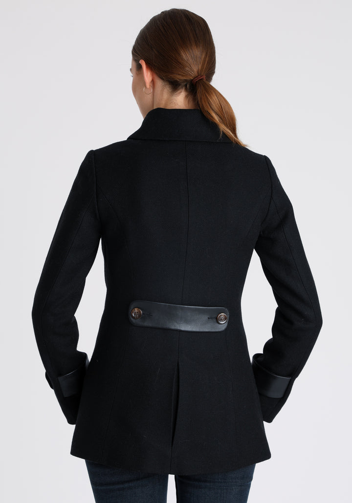 Model wearing the Hendre jacket in black textured wool, a structured style with a high collar, reversible leather cuff bands, and a back belt for versatile styling.