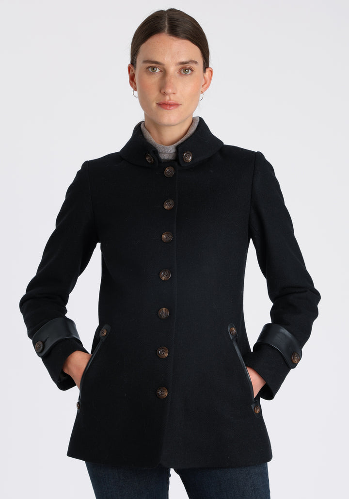 Model wearing the Hendre jacket in black textured wool, a structured style with a high collar, reversible leather cuff bands, and a back belt for versatile styling.