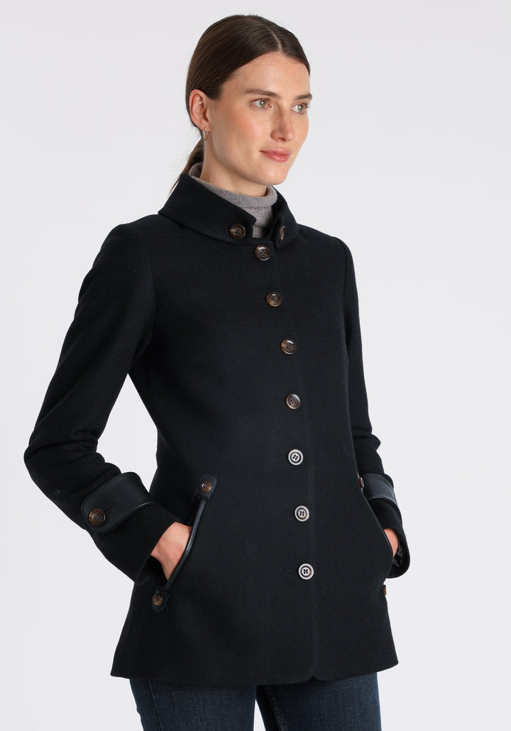 Model wearing the Hendre jacket in black textured wool, a structured style with a high collar, reversible leather cuff bands, and a back belt for versatile styling.