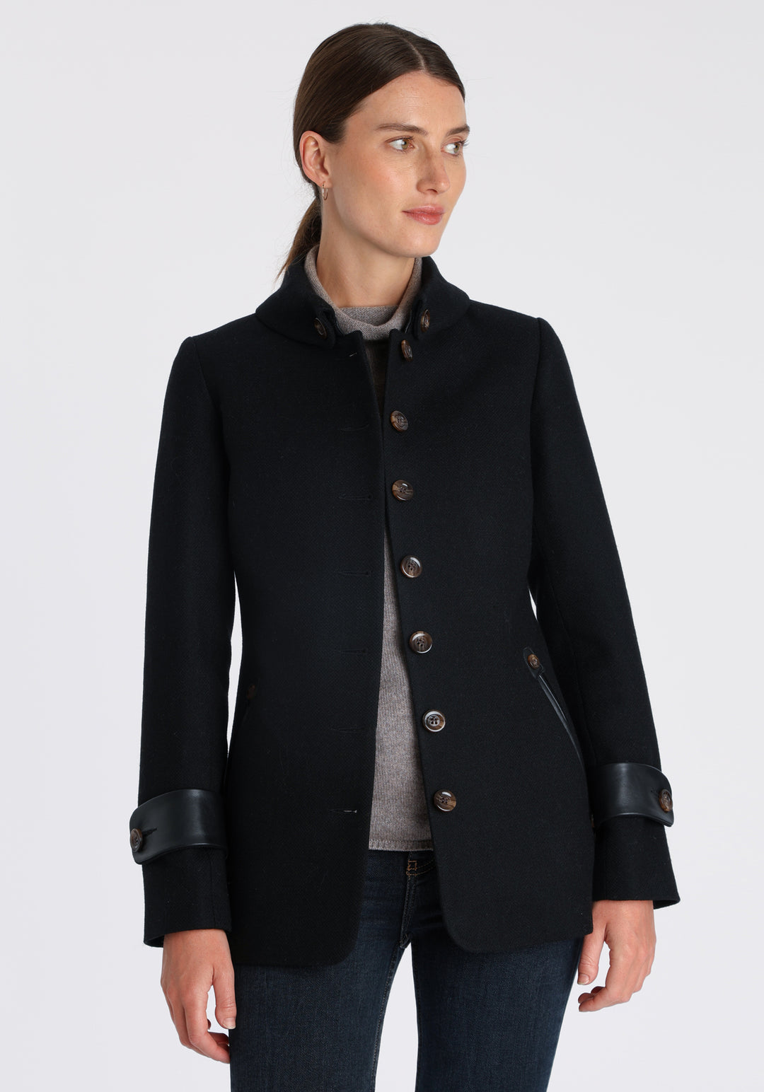 Model wearing the Hendre jacket in black textured wool, a structured style with a high collar, reversible leather cuff bands, and a back belt for versatile styling.