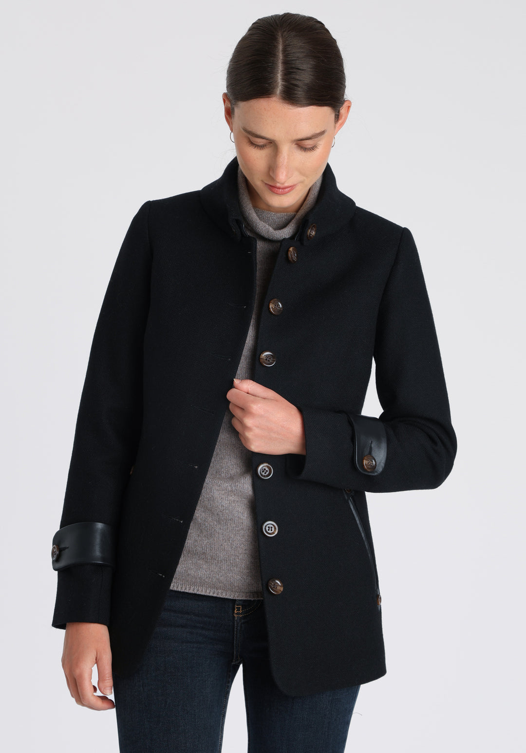 Model wearing the Hendre jacket in black textured wool, a structured style with a high collar, reversible leather cuff bands, and a back belt for versatile styling.