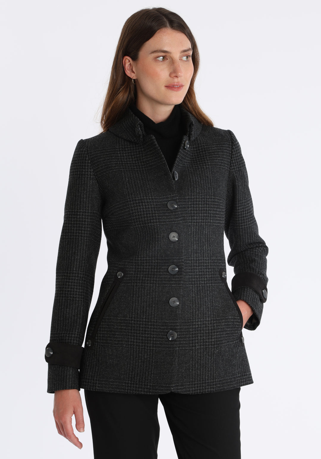 Model wearing the Hendre jacket in black and grey Prince of Wales check, a structured style with a high collar, reversible suede cuff bands, and a back belt for versatile styling.