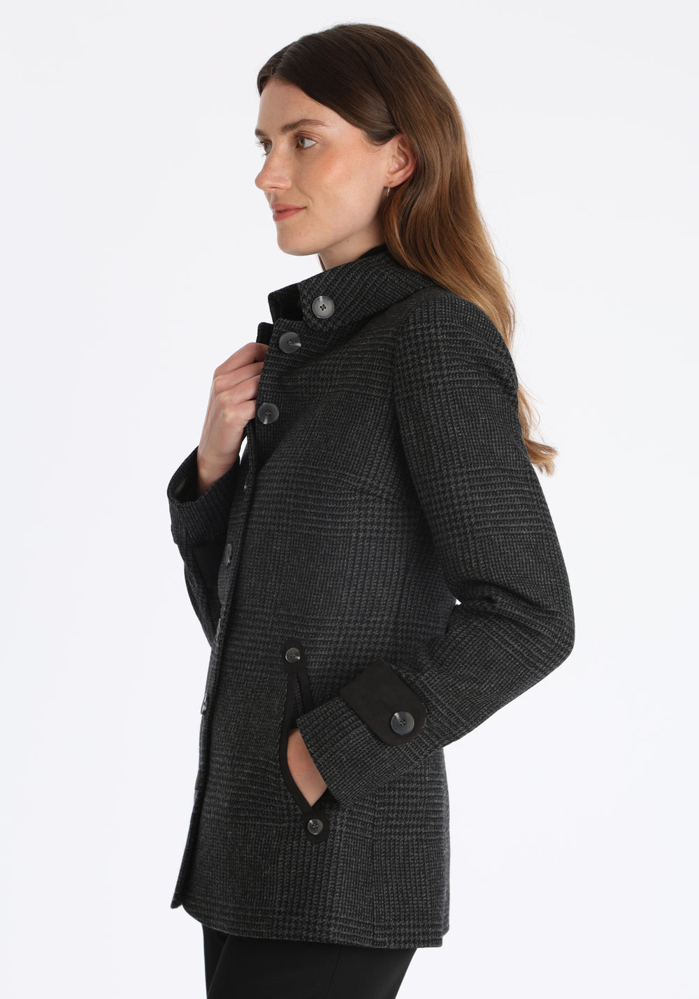 Model wearing the Hendre jacket in black and grey Prince of Wales check, a structured style with a high collar, reversible suede cuff bands, and a back belt for versatile styling.