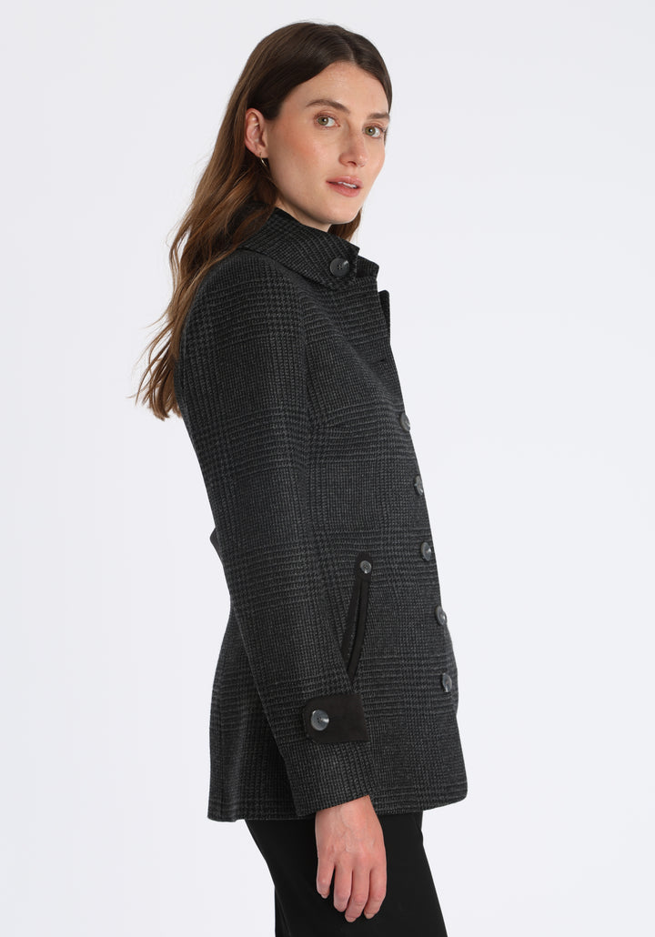 Model wearing the Hendre jacket in black and grey Prince of Wales check, a structured style with a high collar, reversible suede cuff bands, and a back belt for versatile styling.