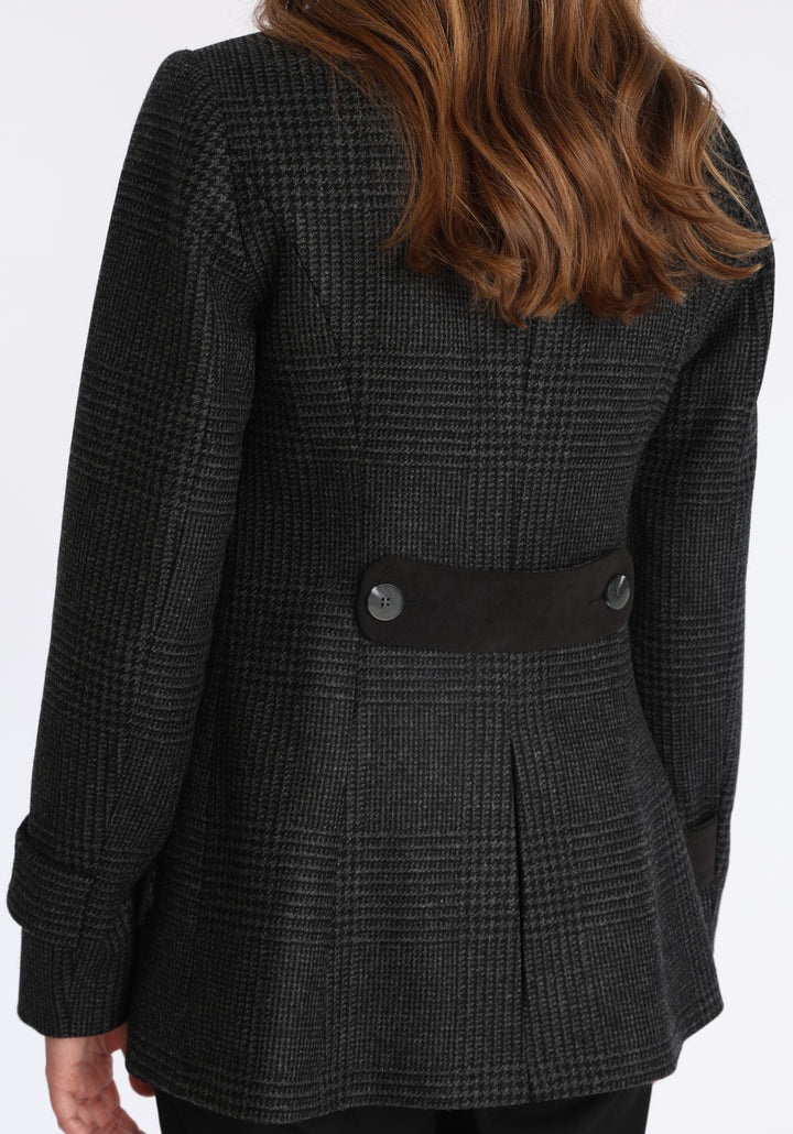 Model wearing the Hendre jacket in black and grey Prince of Wales check, a structured style with a high collar, reversible suede cuff bands, and a back belt for versatile styling.