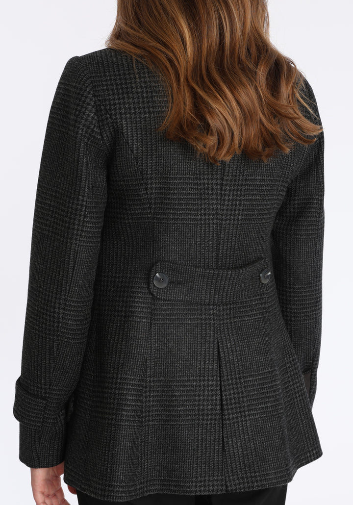 Model wearing the Hendre jacket in black and grey Prince of Wales check, a structured style with a high collar, reversible suede cuff bands, and a back belt for versatile styling.