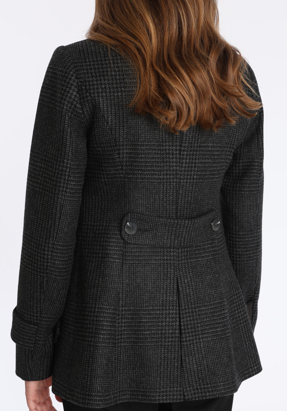 Model wearing the Hendre jacket in black and grey Prince of Wales check, a structured style with a high collar, reversible suede cuff bands, and a back belt for versatile styling.