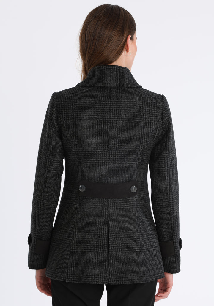 Model wearing the Hendre jacket in black and grey Prince of Wales check, a structured style with a high collar, reversible suede cuff bands, and a back belt for versatile styling.