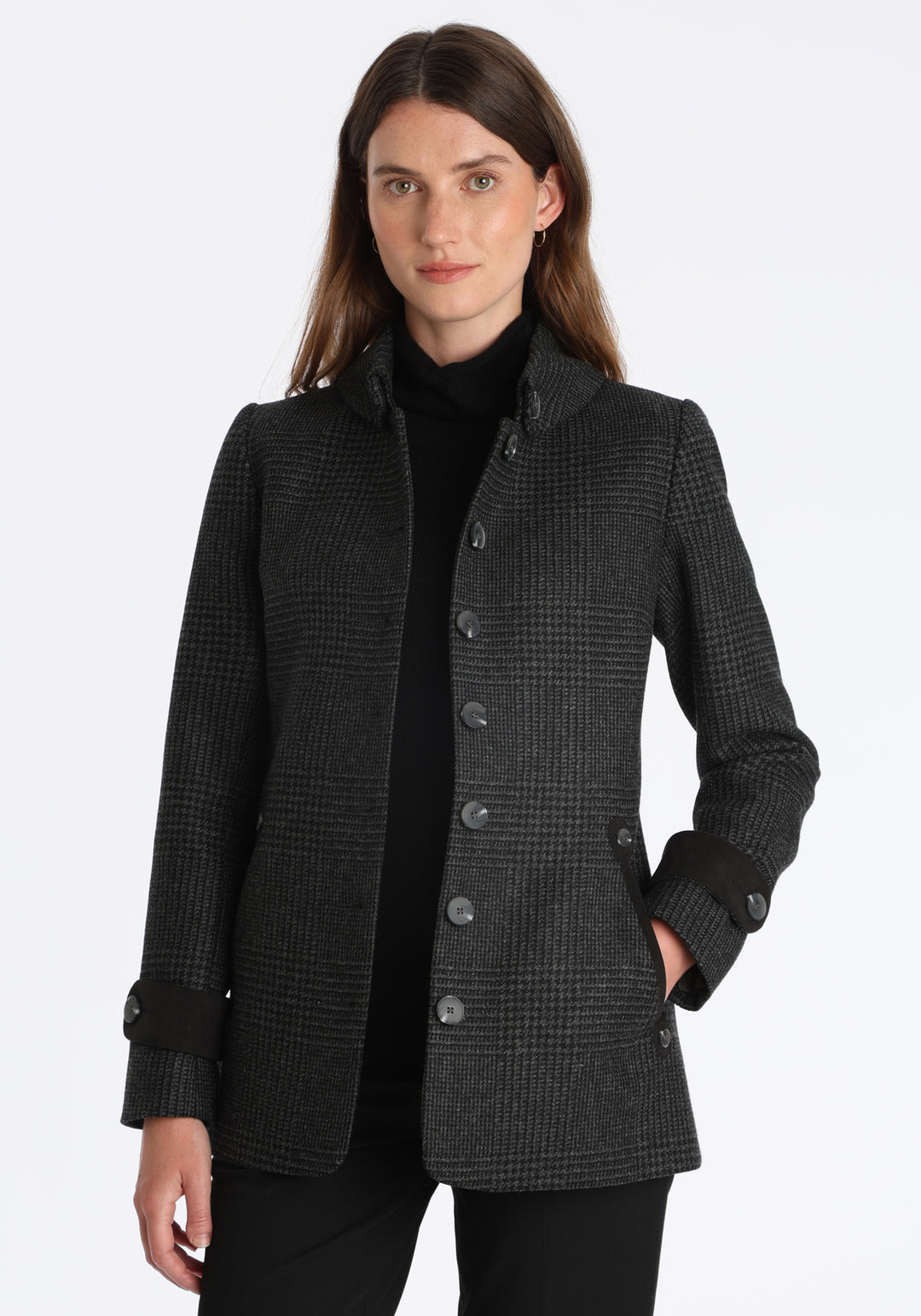 Model wearing the Hendre jacket in black and grey Prince of Wales check, a structured style with a high collar, reversible suede cuff bands, and a back belt for versatile styling.