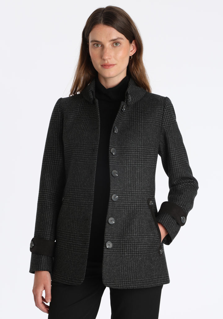 Model wearing the Hendre jacket in black and grey Prince of Wales check, a structured style with a high collar, reversible suede cuff bands, and a back belt for versatile styling.